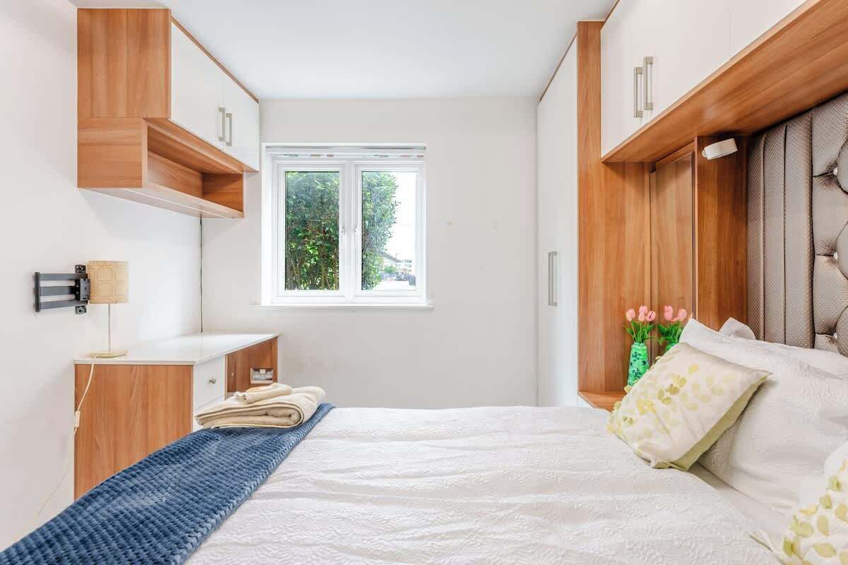 A bedroom with a bed, a window, wooden cabinets, and a bedside table.