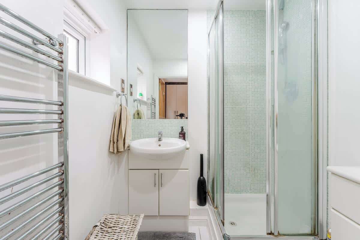 Een badkamer met een douchecabine van glas, een witte wastafel en een metalen handdoekrek.