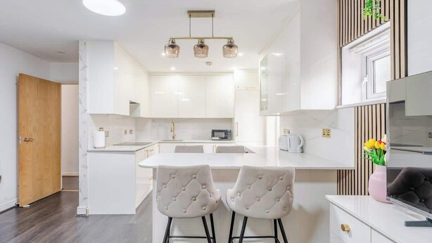 Een moderne keuken met witte kasten, een centraal eiland met twee barstoelen en een houten deur.