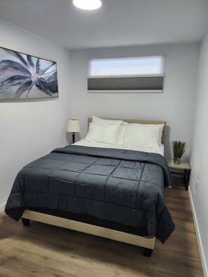 Ein Schlafzimmer mit einem Bett, einer Nachttischlampe, einem Topf mit einer Pflanze und einer Deckenleuchte.