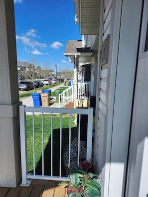 Ein Wohnhaus mit Balkon, einem eingezäunten Garten und freiem Blick auf geparkte Autos und Häuser im Hintergrund.