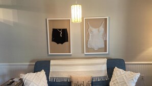 Ett rum med en blå soffa, två kuddar, ett inramat konstverk, en lampa och ett litet bord med en fjärrkontroll.