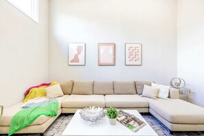 Un salón con un sofá beige, una mesa de centro blanca y tres obras de arte abstracto enmarcadas en la pared.