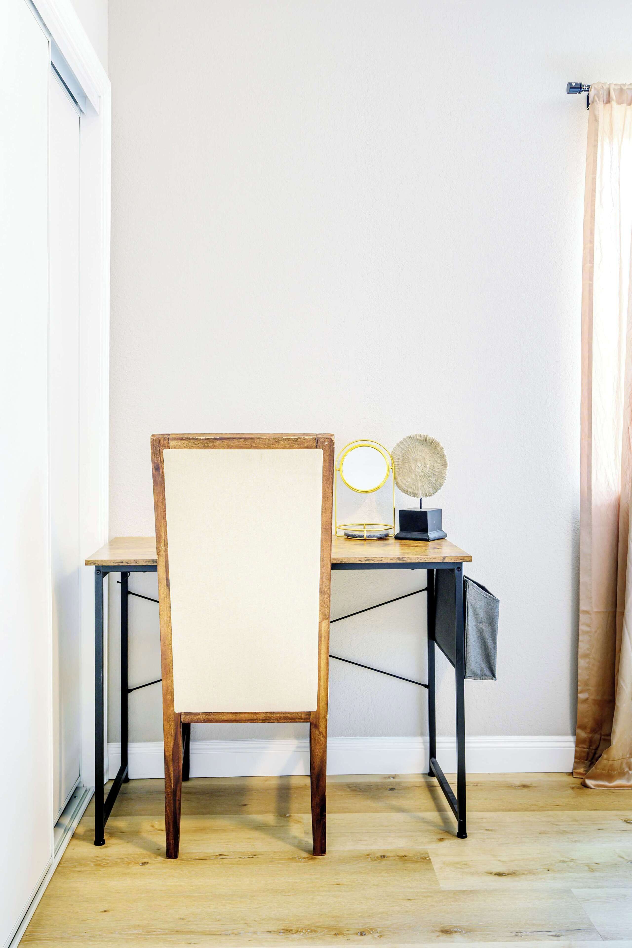 Une pièce d’angle avec une chaise en bois, un bureau avec une lampe et une fenêtre avec des rideaux.