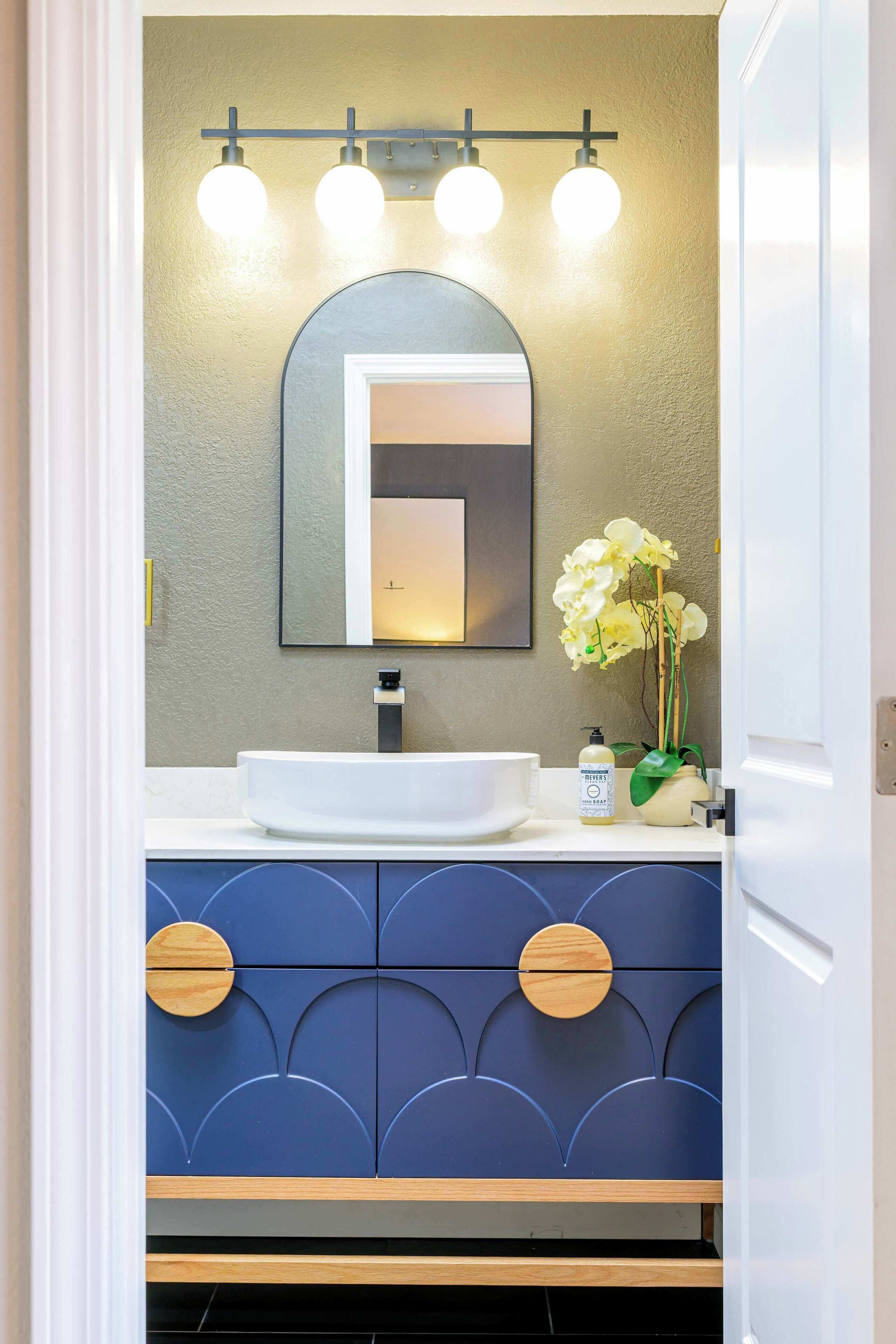 Un baño con un lavamanos blanco, un espejo de marco negro y un mueble de tocador con armarios azules y tiradores de madera.