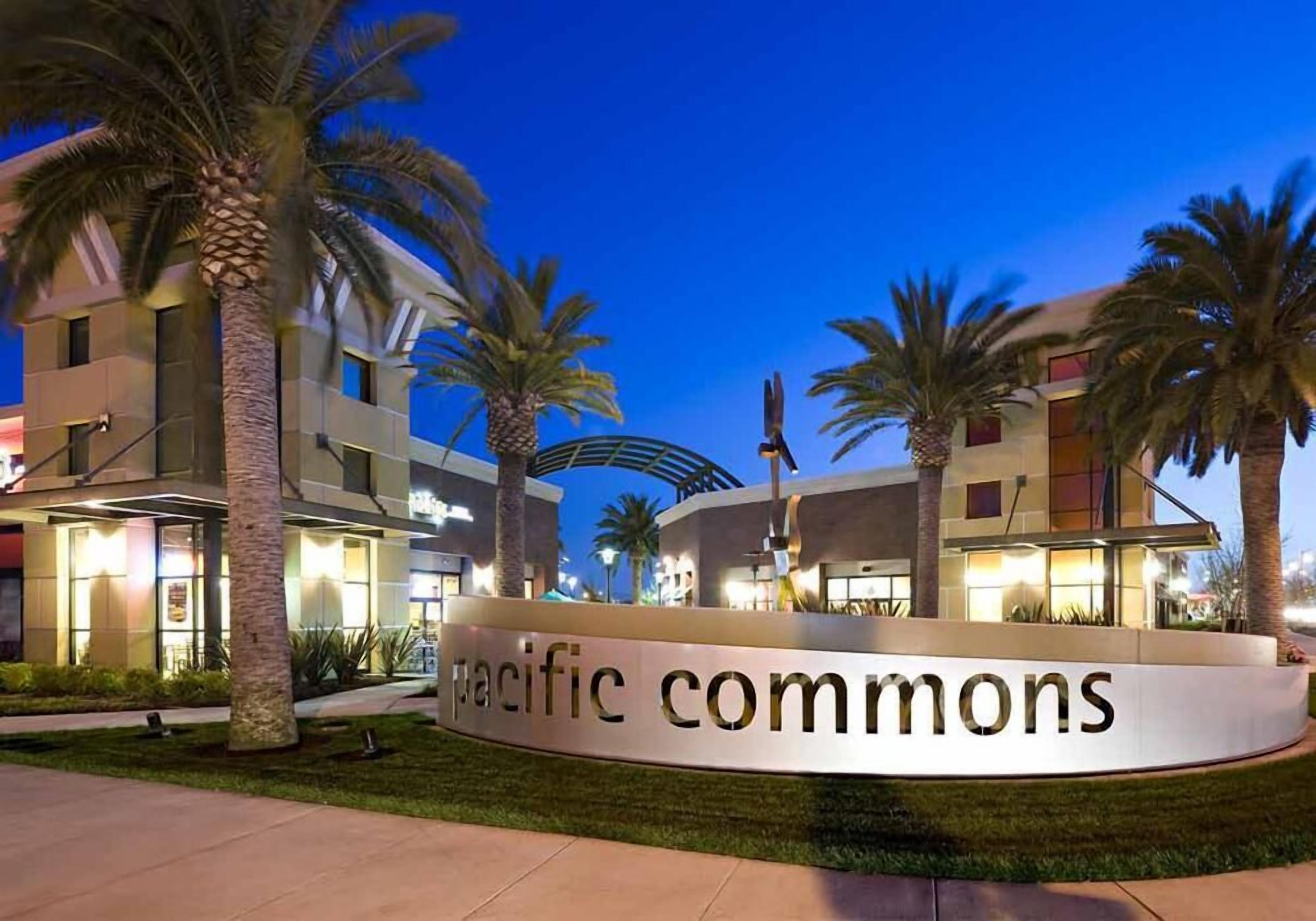 Ein Hotel Eingang mit einem Schild, das 'Pacific Commons' zeigt, umgeben von Palmen und modernen Gebäuden.