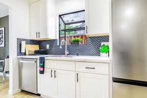 A modern kitchen with white cabinets, a stainless steel refrigerator, a window with a view, and a herringbone-patterned backsplash.