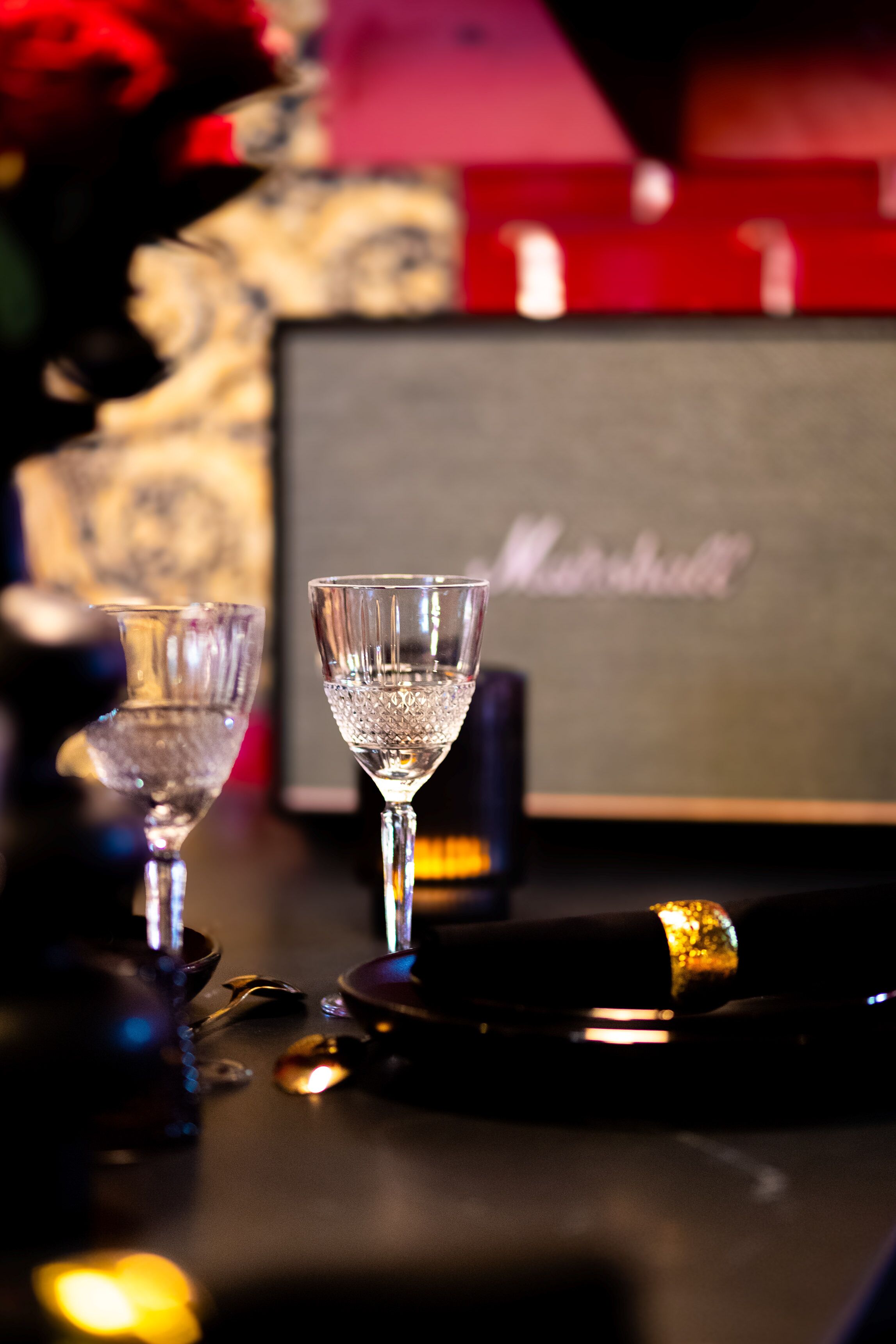 A bar area with two glasses on a table, a bottle, and a sign with the name 'Marshall'.