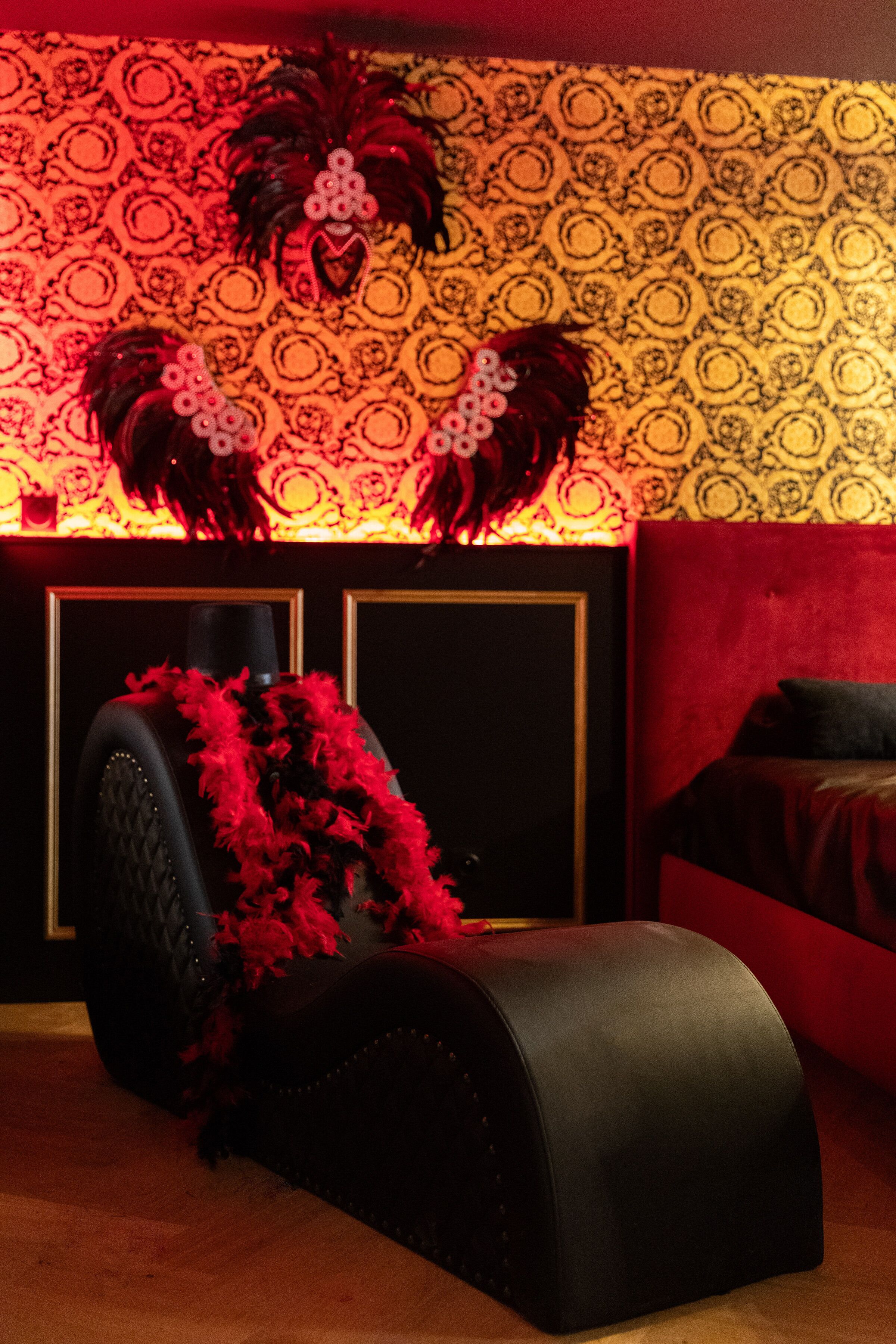 A room with a patterned wallpaper, a black upholstered headboard, and a red accent wall.