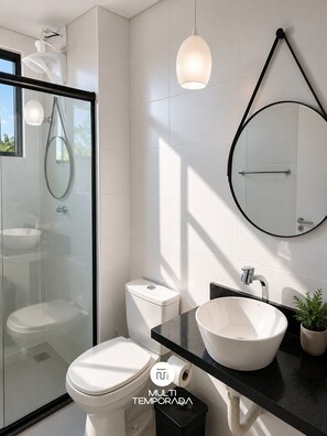 A modern bathroom with a glass shower enclosure, a toilet, a sink with a basin, and a mirror with a black frame.