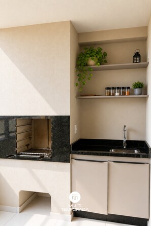 A kitchen with a built-in grill, a sink, and shelves with spices and a potted plant.