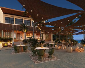 An outdoor seating area with round tables and chairs, surrounded by palm trees and a building with large windows. - Park Hyatt Riviera Maya - All Inclusive (Puerto Morelos)