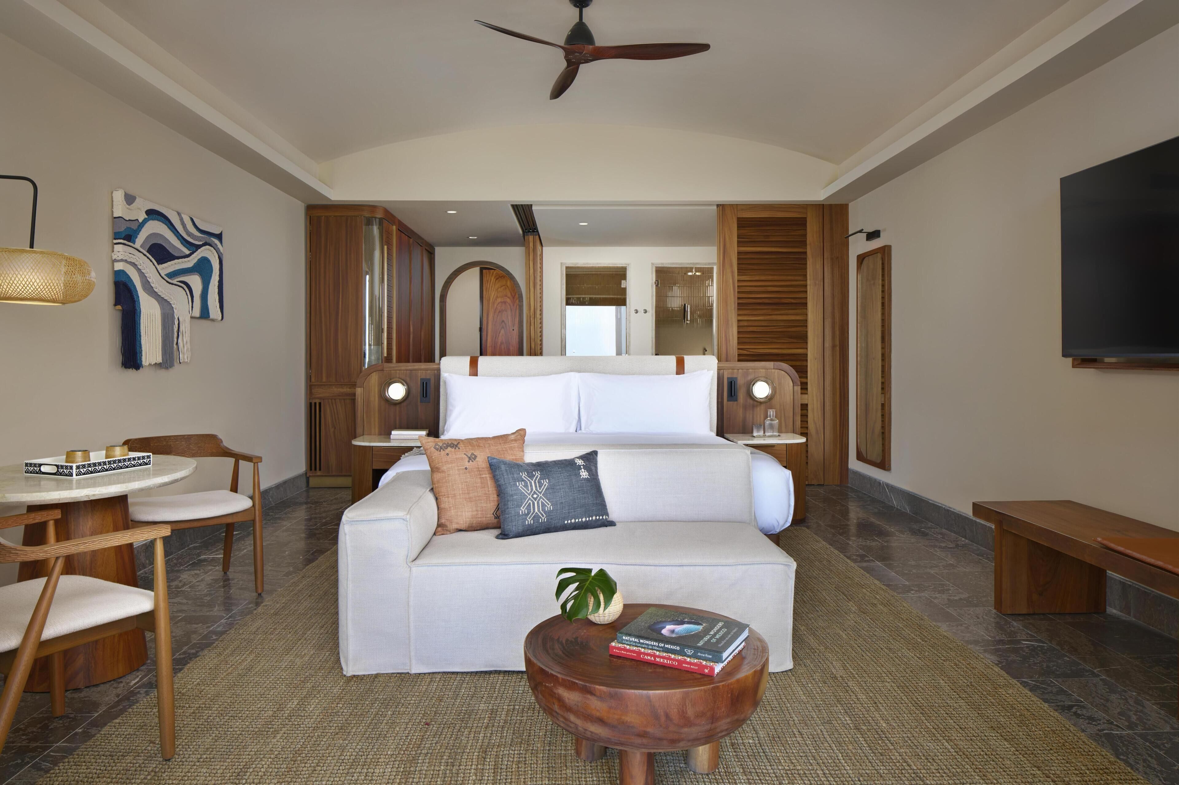 A hotel room with a bed, a sofa, a dining area, and a TV.