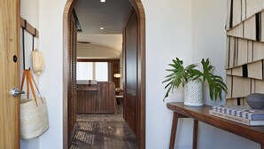 A hallway with a wooden door, a hanging bag, a plant on a table, and a book titled 'EIGHT HOUSES CLEMENTS DESIGN'. - Park Hyatt Riviera Maya - All Inclusive (Puerto Morelos)