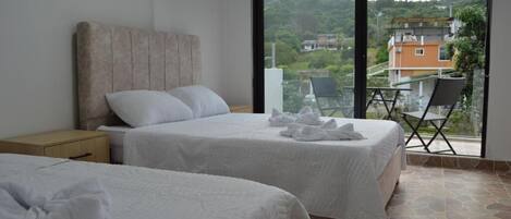 A hotel room with two beds, a large window, and a balcony with a view of the surrounding area.
