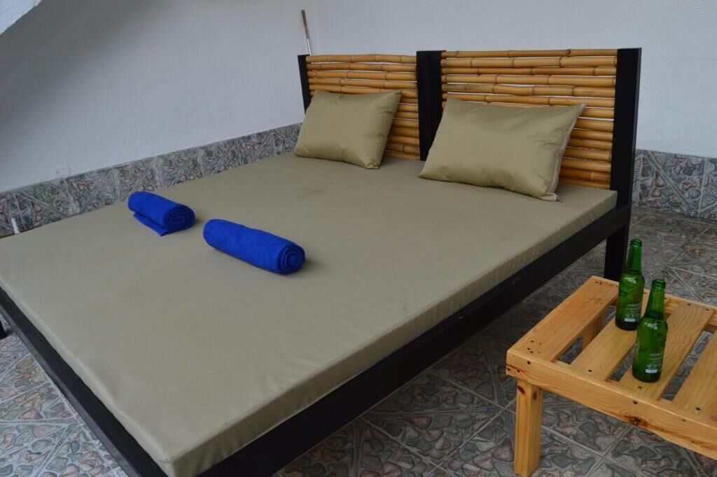 Una cama individual con cabecera de bambú, dos almohadas color beige y un cubrecolchón verde.