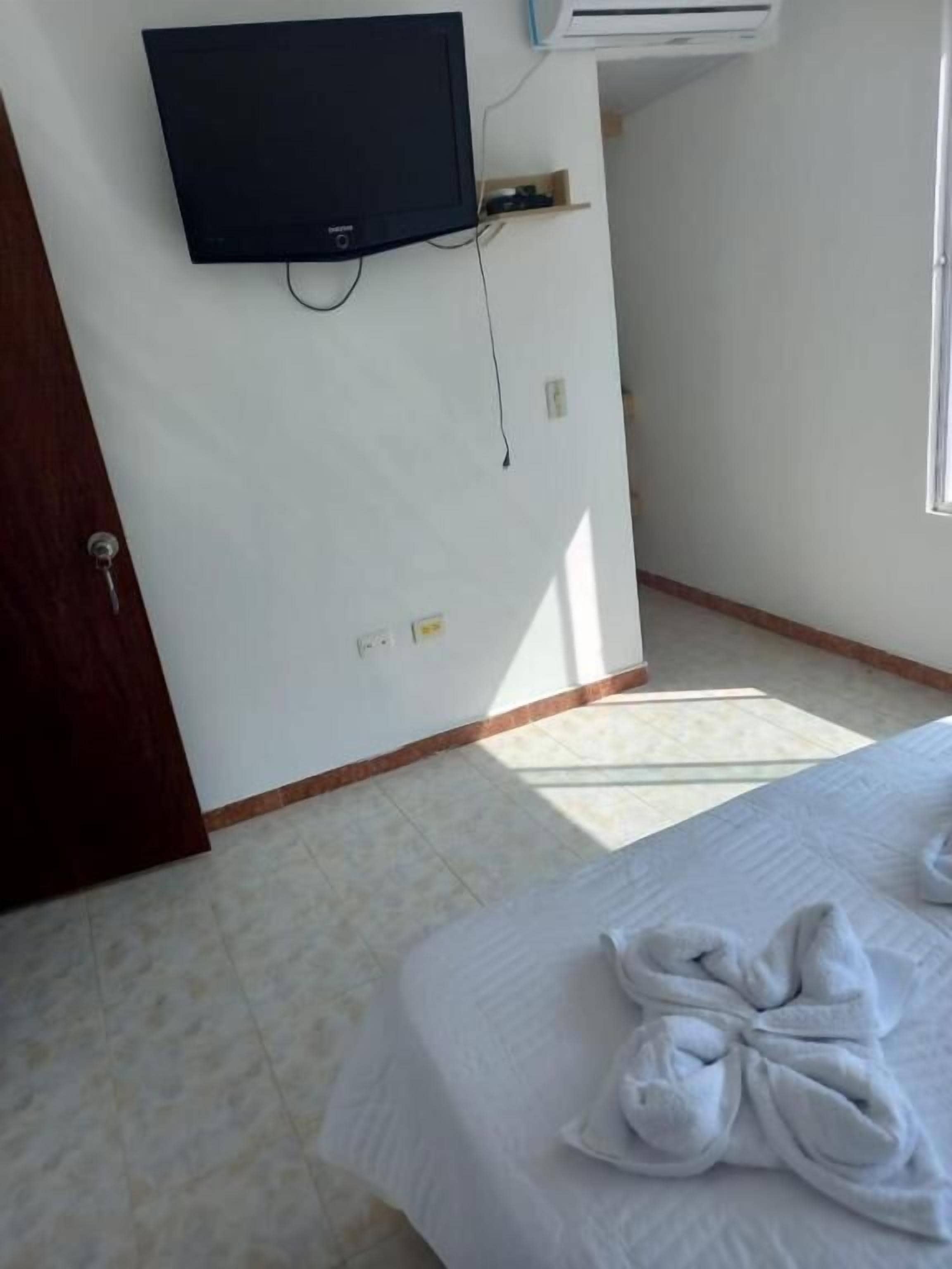 Ein Hotelzimmer mit Bett, einem flachbildfernseher an der Wand, einer kleinen Ablage und einem Fenster.