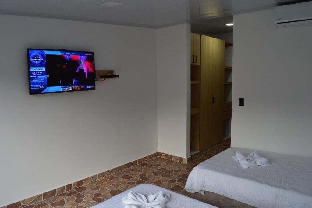 Een hotelkamer met een televisie aan de muur, twee bedden, een vloer met een steenmotief en een houten garderobe.