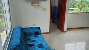 A room with a blue sofa, a flat-screen TV mounted on the wall, and a view of greenery through the window. - hotel guacamayas resort vacation (La Mesa)