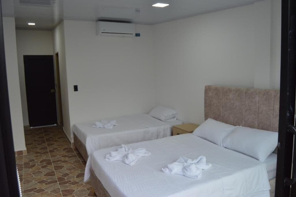 A hotel room with two beds, a nightstand, an air conditioning unit, and a tiled floor.