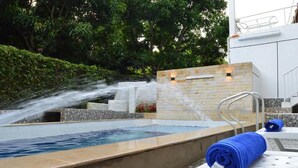A pool with a water feature, a white wall with a light, and a blue towel on a white chair. - hotel guacamayas resort vacation (La Mesa)