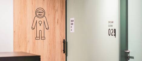A wooden door with a 'Female Only' sign and a figure symbol, and a wall with 'Dream Dorm 01' and 'Dream Dorm 02' signs.