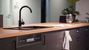 A modern kitchen with a black faucet, wooden countertop, and dark cabinetry. - Dream Factory Hostel Melk (Melk)