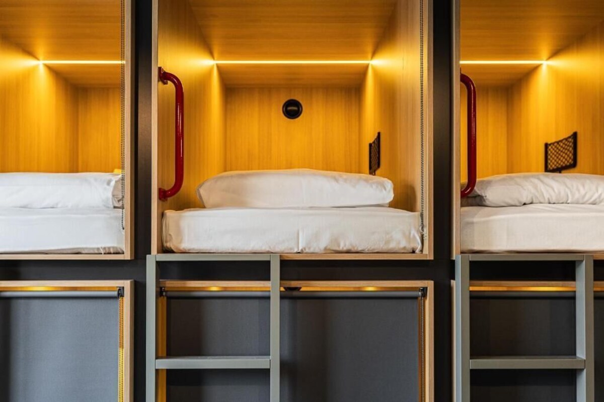 A room with three bunk beds, each with a mattress and pillows, and a wooden wall with a circular light fixture.