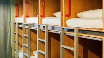 Una hilera de literas con cabeceros de madera y estructuras metálicas, cada una con un agarrador rojo.