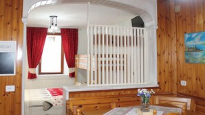 Ein gemütliches Zimmer mit einem Holckrippe, einem Esstisch mit Stühlen, einer Bank und einem Fenster mit roten Vorhängen.