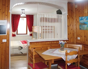 Ein gemütliches Zimmer mit einem Holckrippe, einem Esstisch mit Stühlen, einer Bank und einem Fenster mit roten Vorhängen.