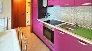 A modern kitchen with pink cabinets, a black countertop, and a tiled backsplash. - Casa Via Vai - Casa in Scalve (Valle Richetti)