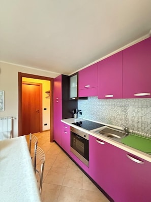 Una cucina moderna con mobili rosa, un piano di lavoro nero e uno schienale piastrellato.