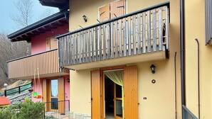 A two-story building with a balcony, a wooden door, and a stone pathway leading to the entrance. - Casa Via Vai - Casa in Scalve (Valle Richetti)