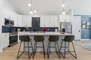 A modern kitchen with white cabinets, a central island with bar stools, a microwave, oven, and a refrigerator. - Luxury Coastal Family Retreat-Fire Pit, Game Room, Walk to Beach, Kid Friendly! (Gulfport)