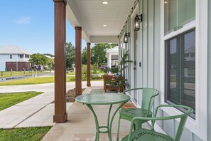 A covered patio with a table and chairs, a view of the street, and a building with a large window. - Luxury Coastal Family Retreat-Fire Pit, Game Room, Walk to Beach, Kid Friendly! (Gulfport)