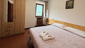 Et soveværelse med en seng, et træskab, et vindue med gardiner, en radiator og et billede hængt på væggen.