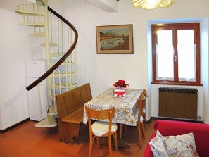 A dining area with a spiral staircase, a table with a floral tablecloth, and a window with curtains. - Cottage di Maria - Casa in Scalve (Grana)