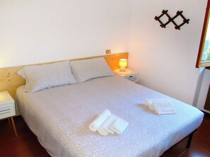 A neatly made bed with a patterned bedspread, two pillows, and a bedside lamp. - Cottage di Maria - Casa in Scalve (Grana)