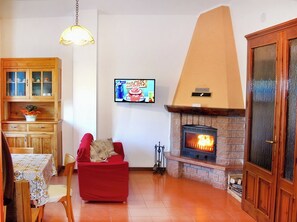 Un salon avec une cheminée, un téléviseur et un coin repas comprenant des meubles de rangement en bois et une table.