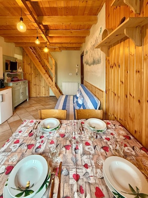 Ein Essbereich mit einem Holztisch, gedeckt für vier Personen, einer Treppe und einer Küche im Hintergrund.
