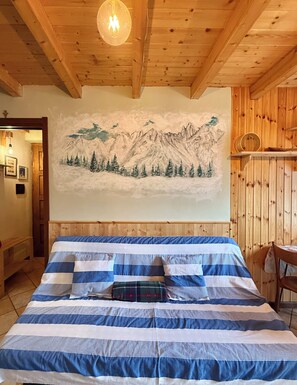 Ein Zimmer mit Holzboden, einem Bett und einer Wandmalerei von Bergen.
