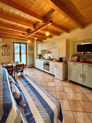 Een gezellige keuken met houten balken, een eethoek met een tafel en stoelen, en een bed met gestreepte beddengoed.