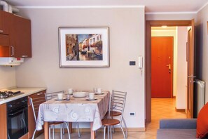 A dining area with a table set for four, a kitchen with a stove and oven, a framed picture of a canal, and a door leading to another room.