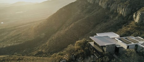A modern building with a flat roof, surrounded by steep hills and dense vegetation.