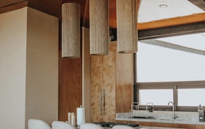 A modern kitchen with a central island, pendant lights, and a large window.