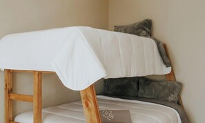 A bunk bed with a white sheet and a pillow, a wooden frame, and a small bedside table with a book.