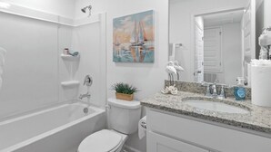 Un baño moderno con bañera, inodoro, lavamanos y un cuadro de veleros.
