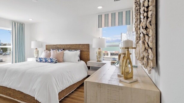 Un dormitorio con cama, mesitas de noche, lámpara, una obra de arte en la pared y vista al mar.