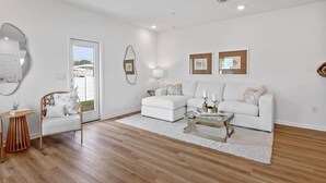 Una sala de estar moderna con un sofá blanco, una mesa de centro, una mesita auxiliar redonda de madera y un espejo.